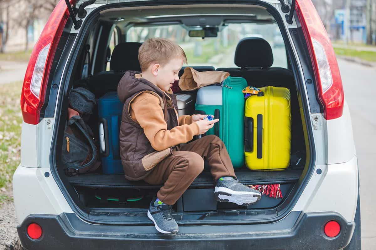 Little kid looking into paper bag with candies sitting in car trunk