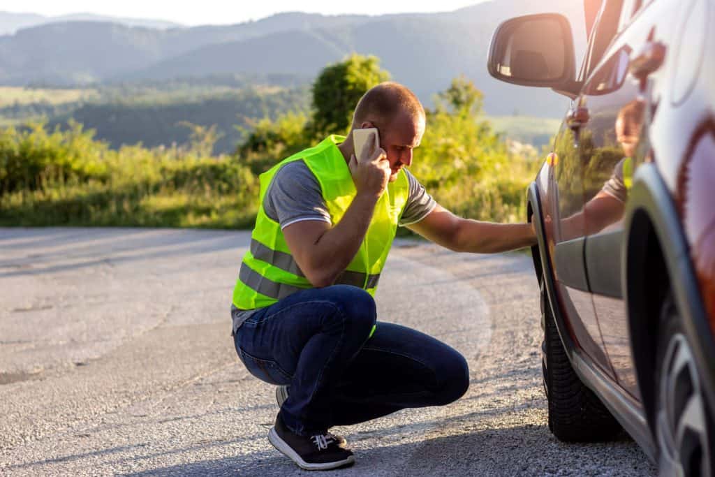Man looking at a broken down car and using mobile for help.