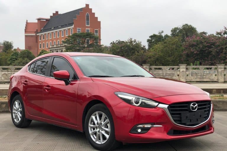 Mazda 3 is park on the street with beutiful orange building in the back, How Often Should You Service A Mazda 3? [Inc. Oil Change]