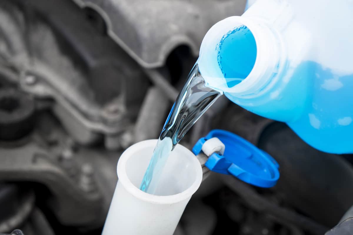 Pouring liquid from plastic canister into car washer fluid reservoir. Close up filling windscreen water tank with washing liquid.