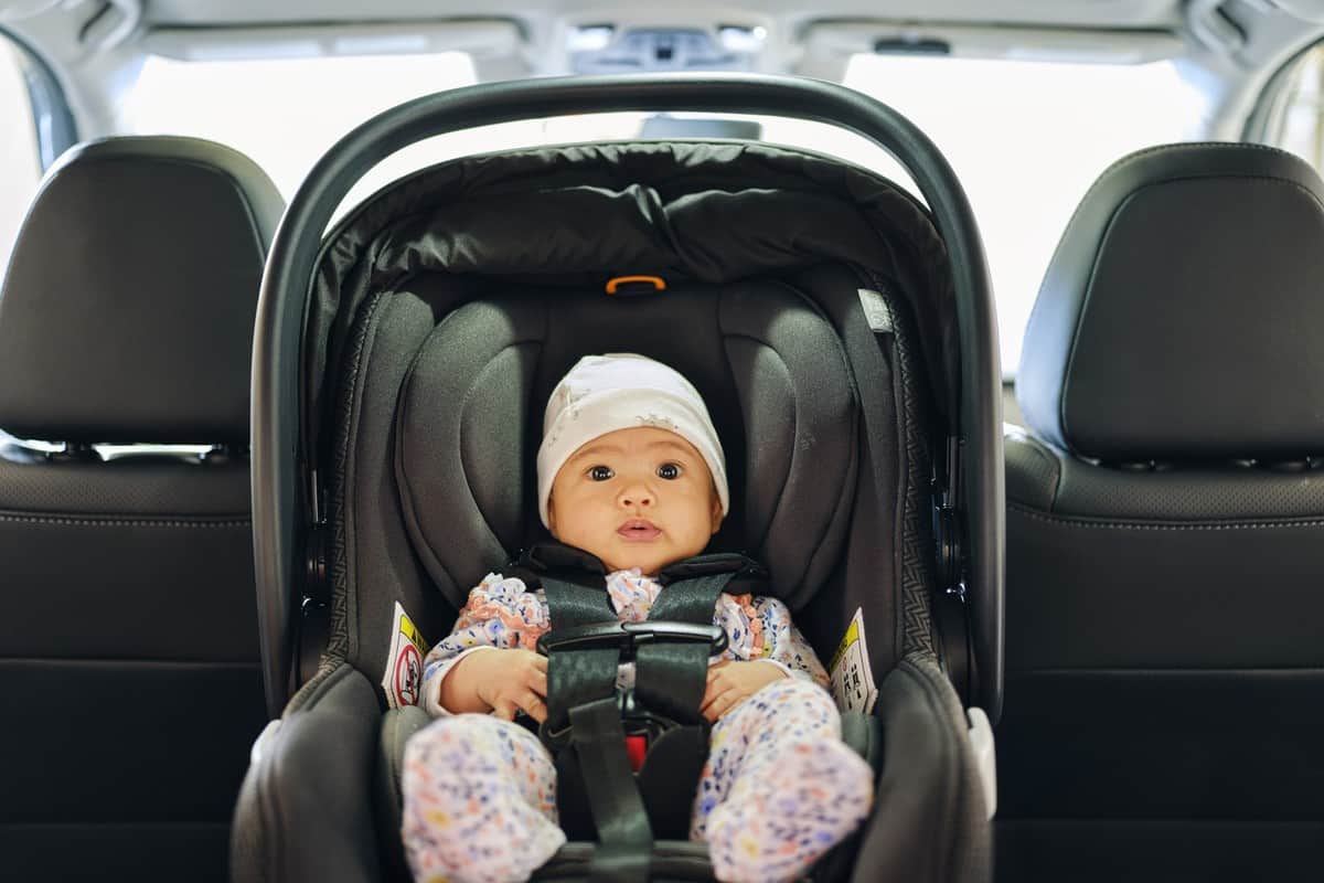 A 3 month old baby sitting in a carseat in the backseat of an auto.
