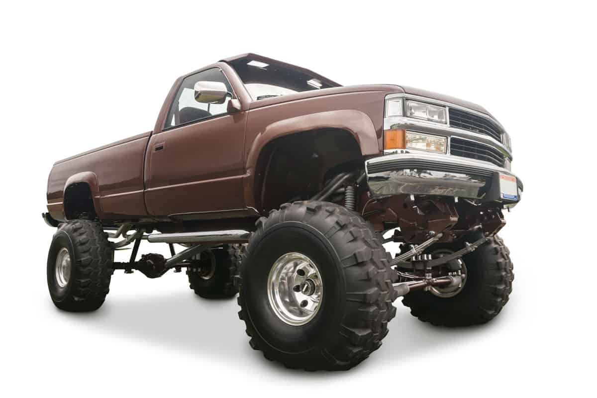 A huge modified truck with huge lug tires for off roading on a white background