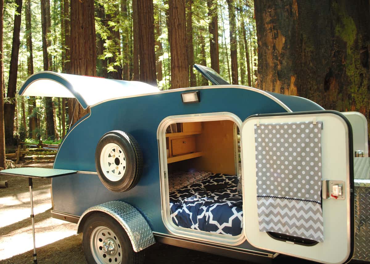 Blue teardrop camping trailer with doors open and view to interior, setup at a campsite surrounded by redwood trees in Humboldt Redwoods State Park in California