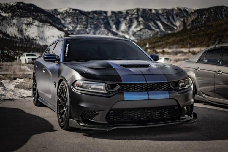 A black with blue stripes Dodge Charger Hellcat parked infront of snow mountains, Dodge Charger Trim Levels And Packages Explained
