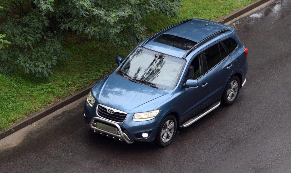 Blue Hyundai Santa Fe is driving along the road in the forest