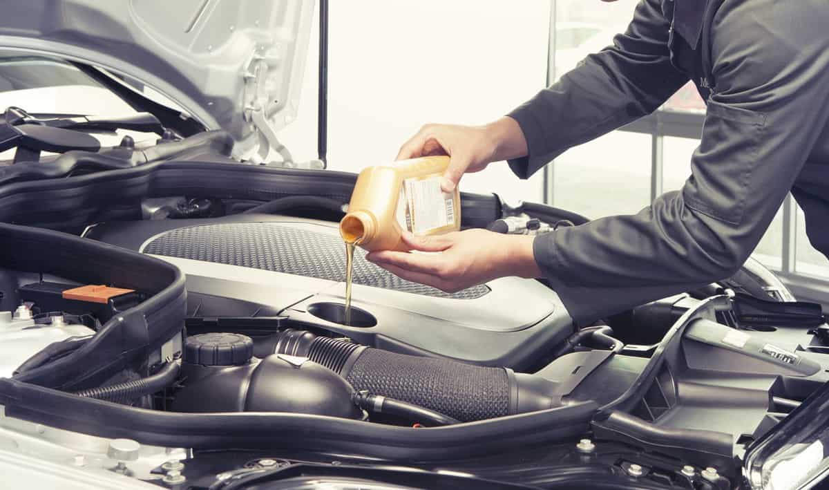 Car mechanic replacing and pouring oil into engine at maintenance repair service station