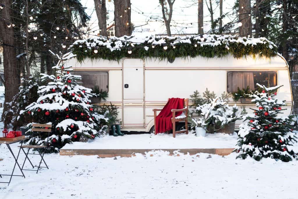 Caravan mobile home with terrace and snow. Mobile home decorated with Christmas decor. 