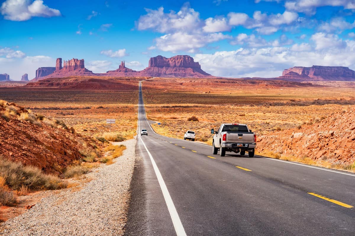Cars drive at Forrest Gump Point in Monument Valley, Utah, USA on a sunny day