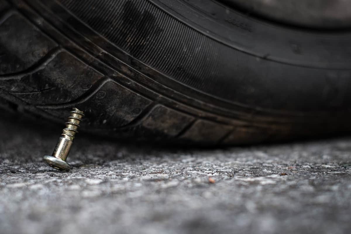 Close up button head needle metal screw nail stuck to puncture into wheel tire on the road