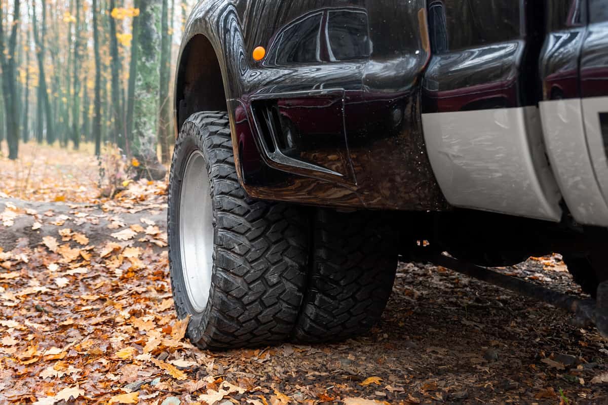 Close-up detail bottom pov view of dual twin offroad performance wheel of super heavy duty pickup truck car at autumn forest countryside driveway. 