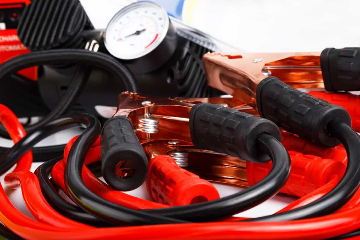 Close up low angle on a coiled set of red and black starter cables or jump leads and a pressure gauge for a car.