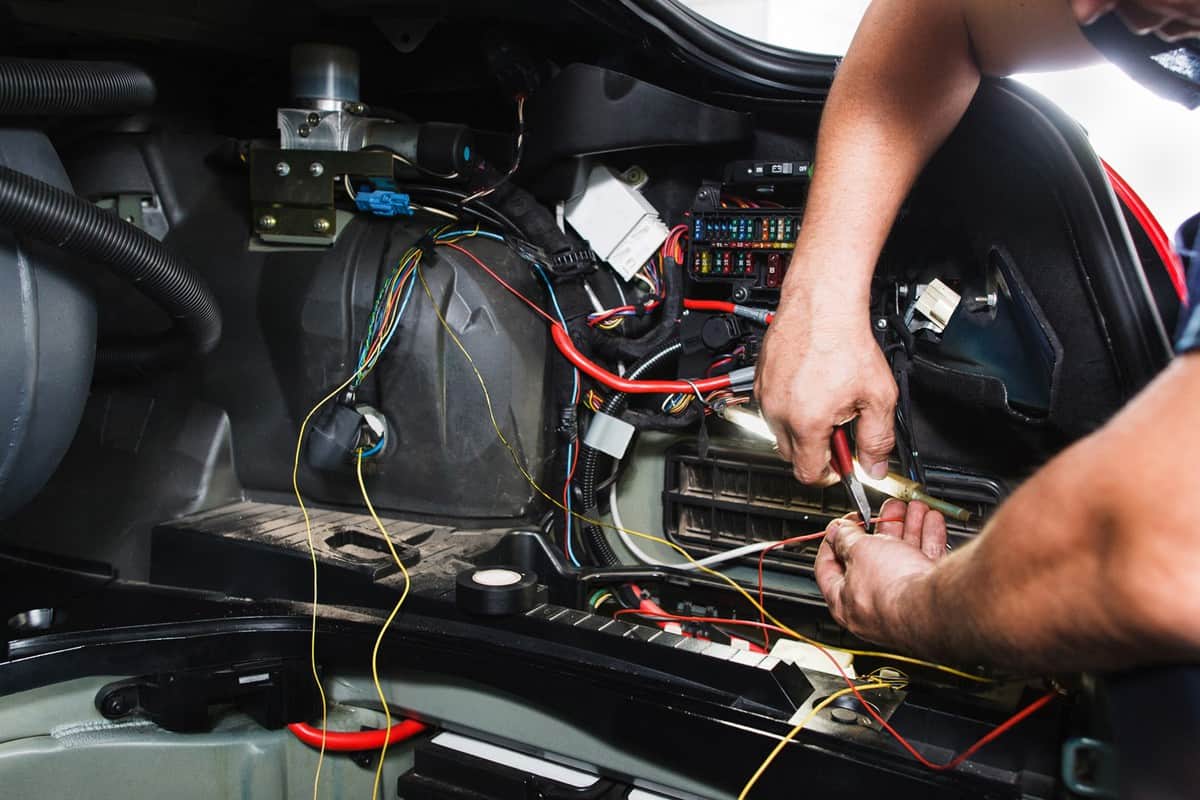 Electrician works with electric block in car. Close-up of automobile inside under raised hood. Service man hands working with cables of auto