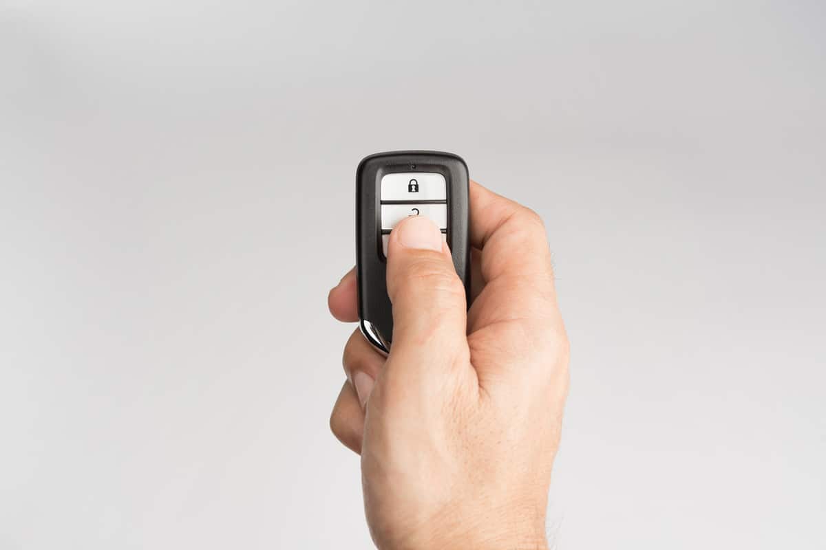 Hand of man holding and push remote control of car to lock unlock or start isolated on gray background