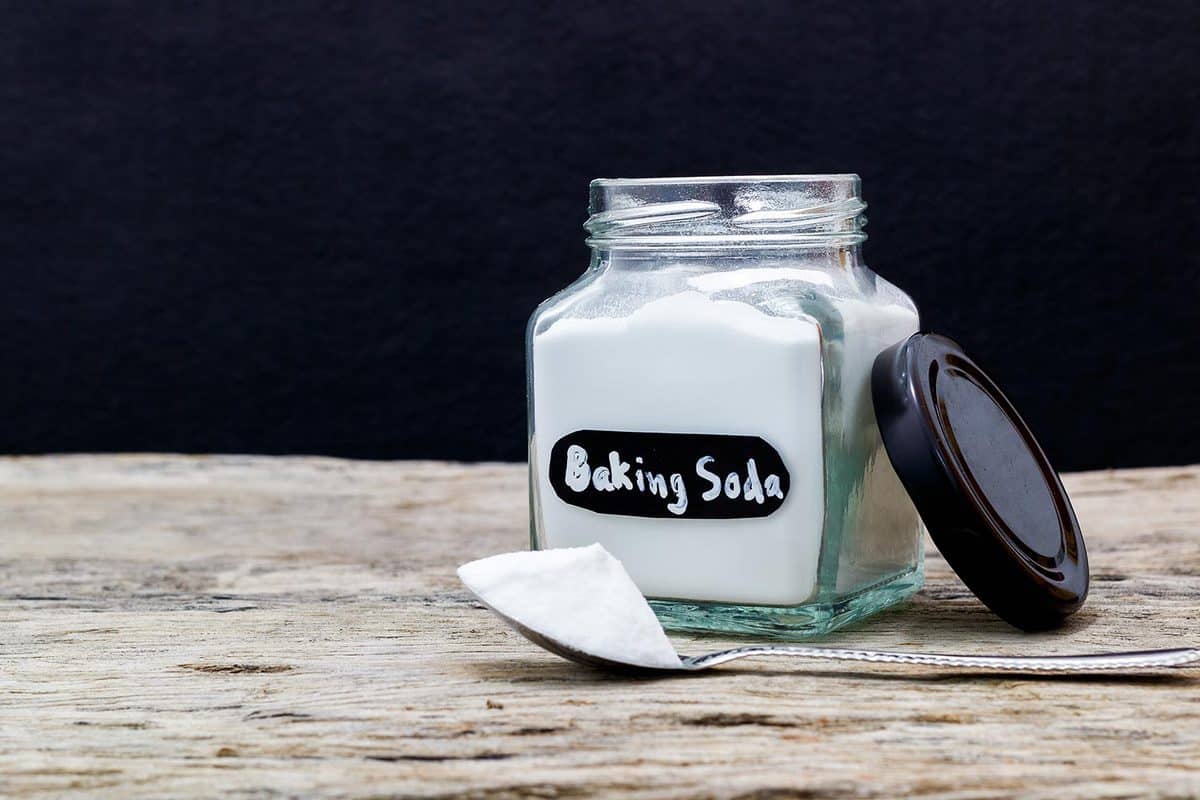 Jar and spoonful of baking soda on wooden table