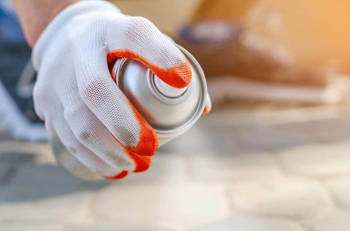 Male hand in a glove holds an aerosol spray can with white paint