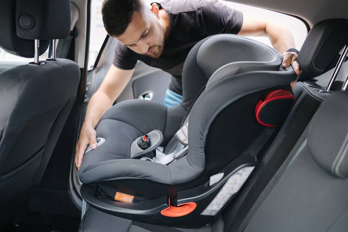 Man installs a child car seat in car at the back seat.