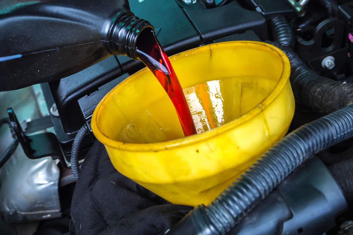Mechanic pouring a container full of transmission fluid to the engine
