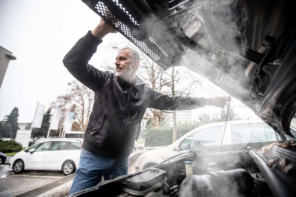 Steam coming out of car engine while mature man is opening the hood