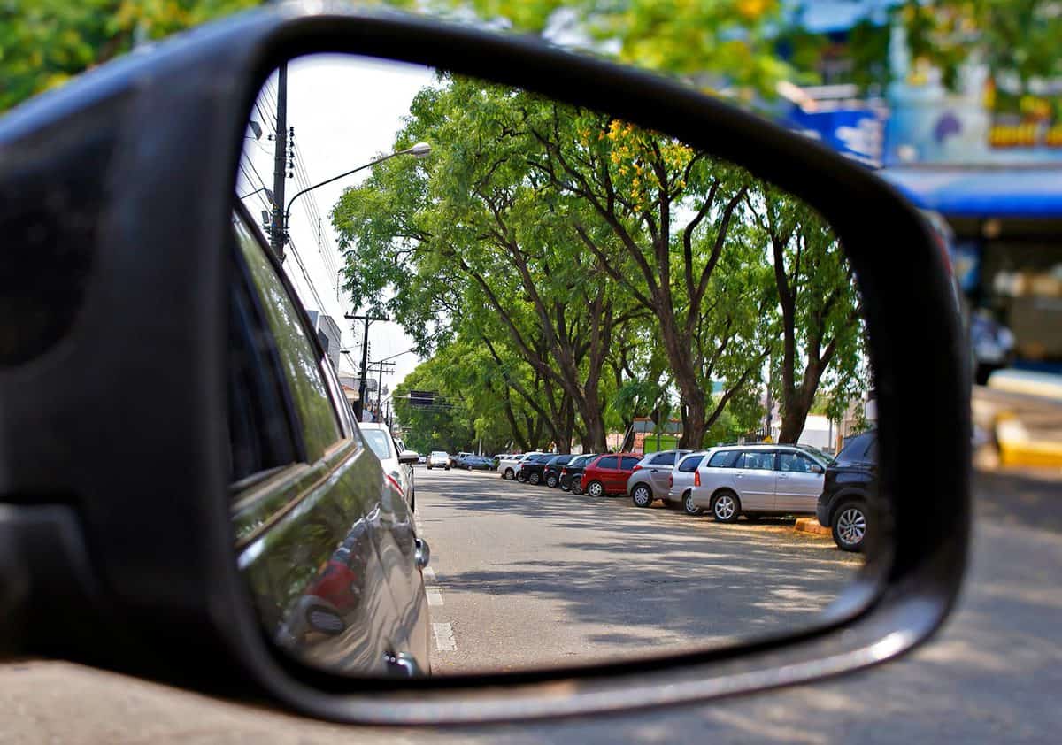 View of many cars parked by the rear view mirror in a small city