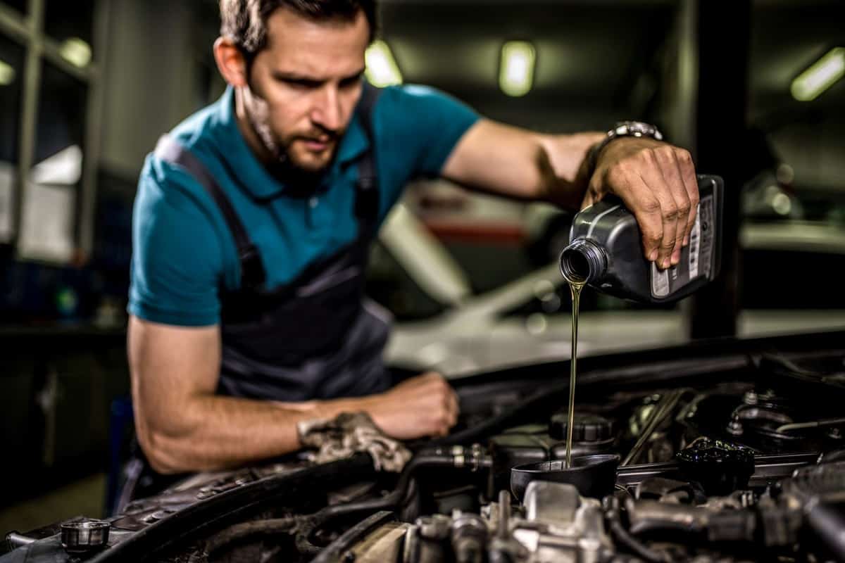 Young auto mechanic changing oil on car engine at auto mechanic shop.
