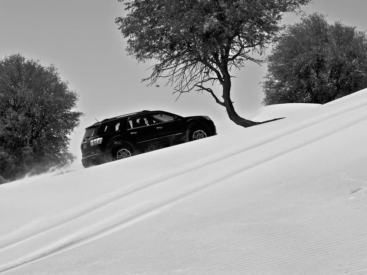 a black car drives up a dune in the desert, off road