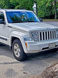 A 2010 Jeep Liberty parked in a wooded area, near a huge pile of sand - Jeep Liberty Stuck In 4WD - What To Do