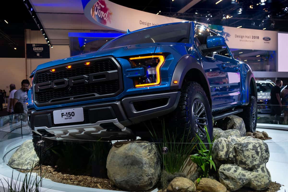 A blue Ford F150 crawling on artificial terrain at a car show