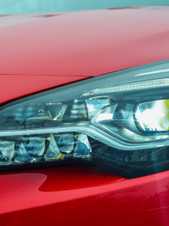 A red car headlight photographed on detail, Headlights And Dash Lights Flicker While Driving—What's Wrong?