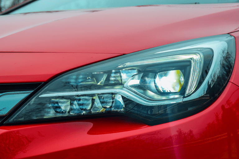 A red car headlight photographed on detail, Headlights And Dash Lights Flicker While Driving—What's Wrong?