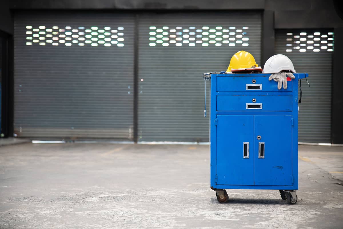 Blue metal tool cabinet with safety helmets, glove, document pad on the cabinet with garage background.