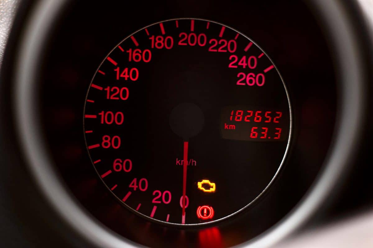 Car dashboard speedometer with check engine light symbol glowing red