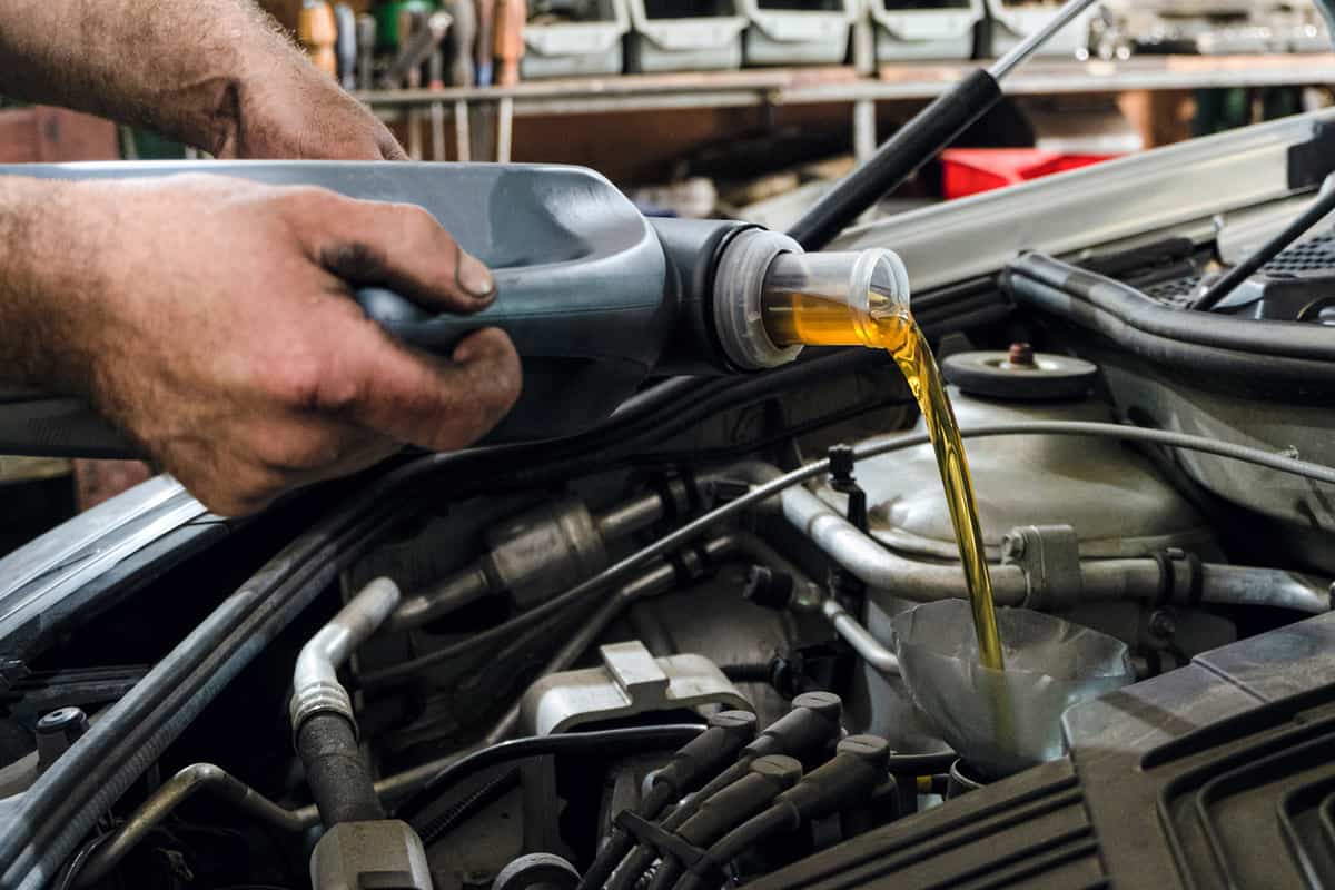 Car mechanic fills motor oil into a car engine