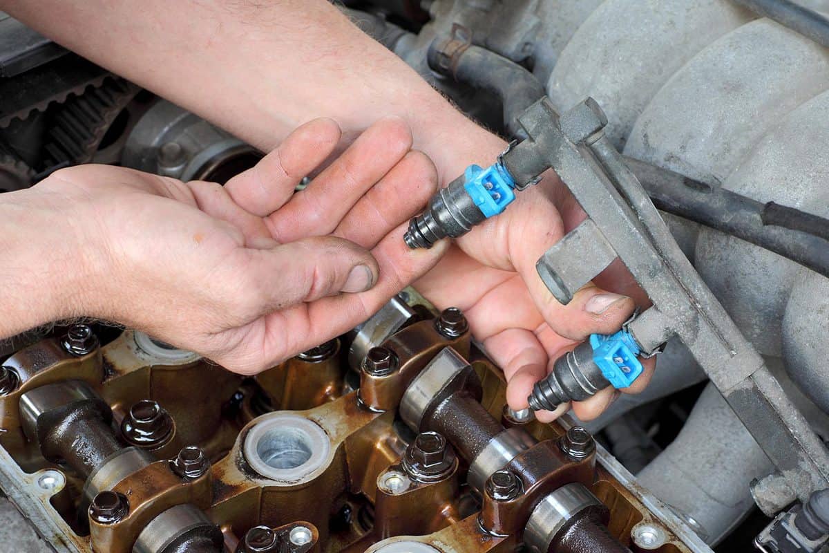 Car mechanic fixing fuel injector at two camshaft gasoline engine