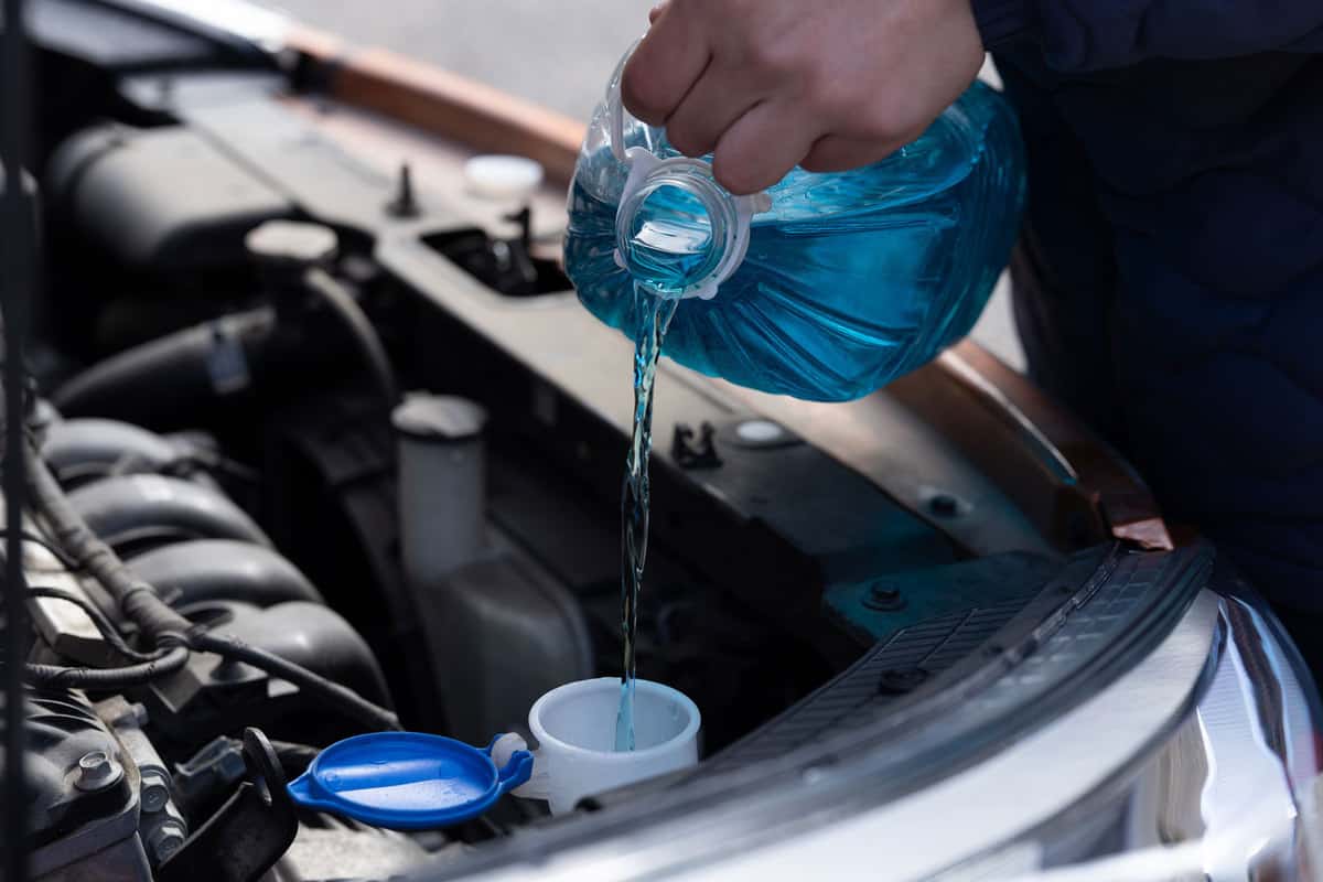 Car mechanic pouring new blue coolant to the engine