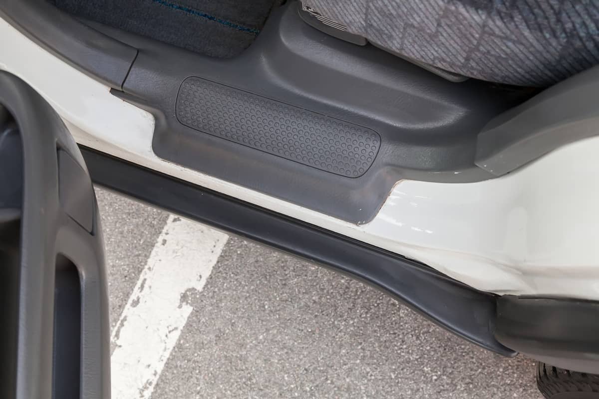 Close-up of a car running board with an open door with a gray plastic trim 