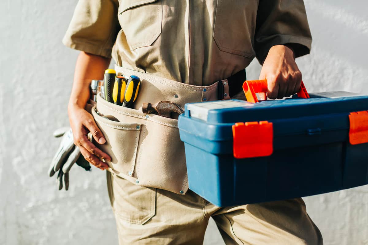 Close-up of repair woman wearing a tool belt holding a toolbox. 