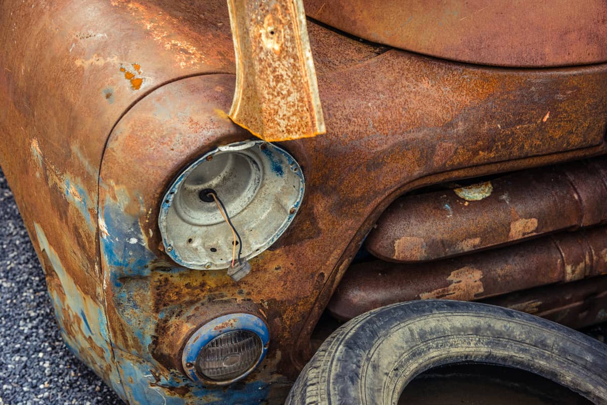 Detail of the front headlight of an rusty car in garage