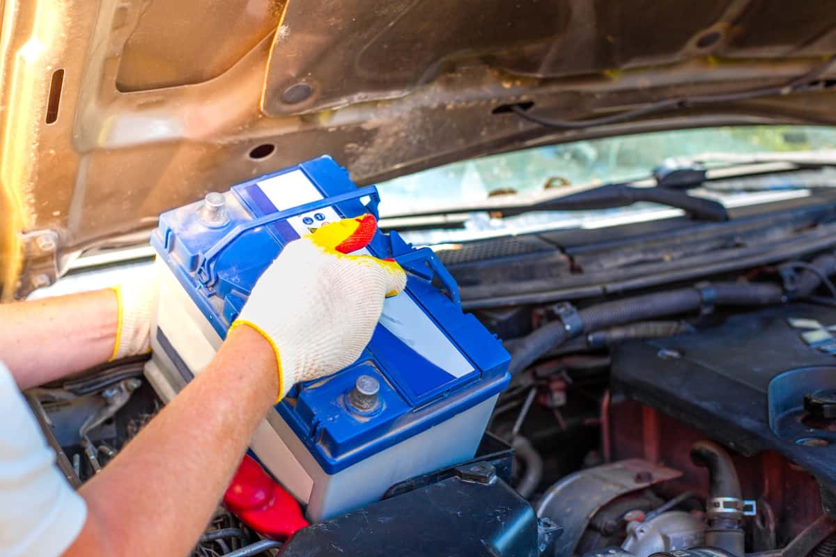 Maintenance of the machine. A male car mechanic takes out a battery from under the hood of a auto to repair, charge or replace it.