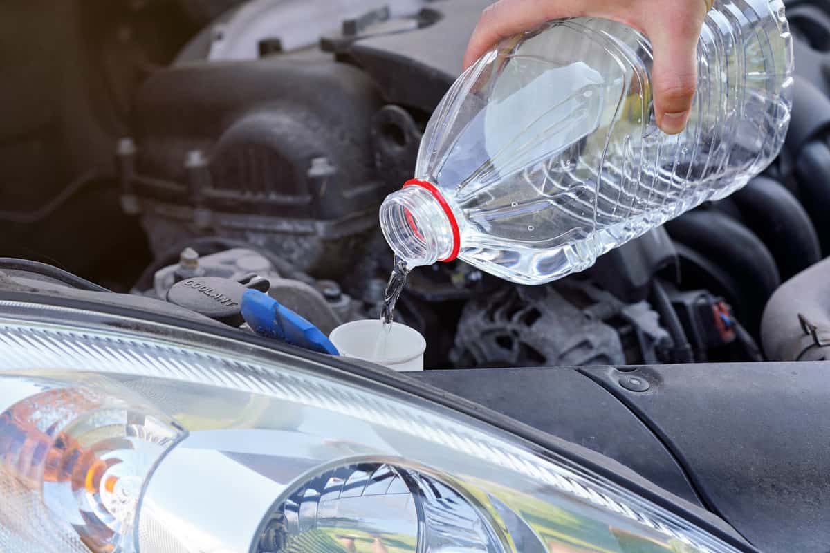 Man pouring distilled water (ecological alternative to washing fluid) to washer tank in car, detail on hand holding clear plastic bottle