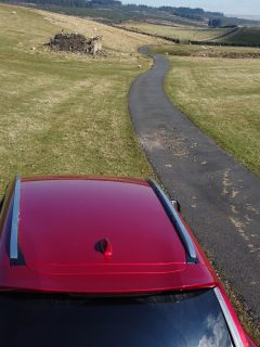 Red car parked on the side of the road with a scenic background, How To Fix A Caved In Car Roof [5 Ideas To Try]