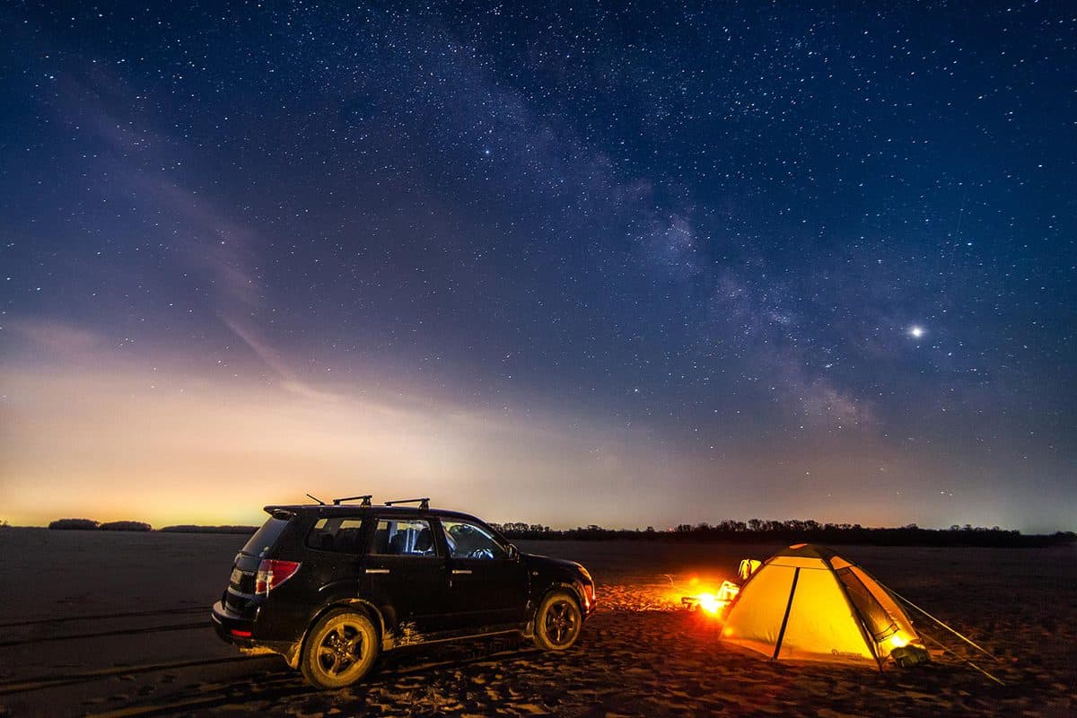 Tourist camping and black crossover under night sky and the Milky Way