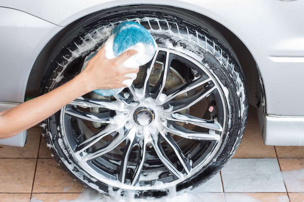 Woman using a blue sponge to clean the rims of the car