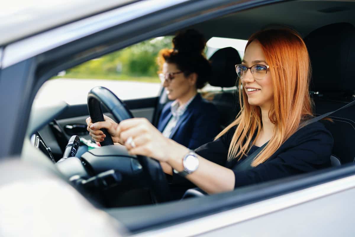 Young and beautiful redhead woman having driving school class with her female instructor.