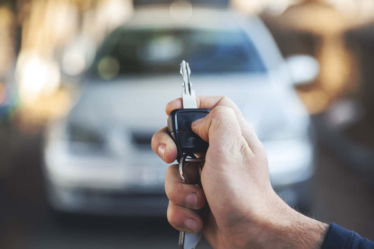 man hand holding key with car in street