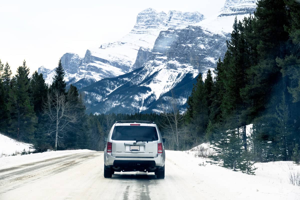 a: A Honda Pilot SUV 4WD is driving on a icy road in the surroundings of Banff, a town located in Banff National Park.View on the snow covered mountains and car through the windshield of the vehicle behind.