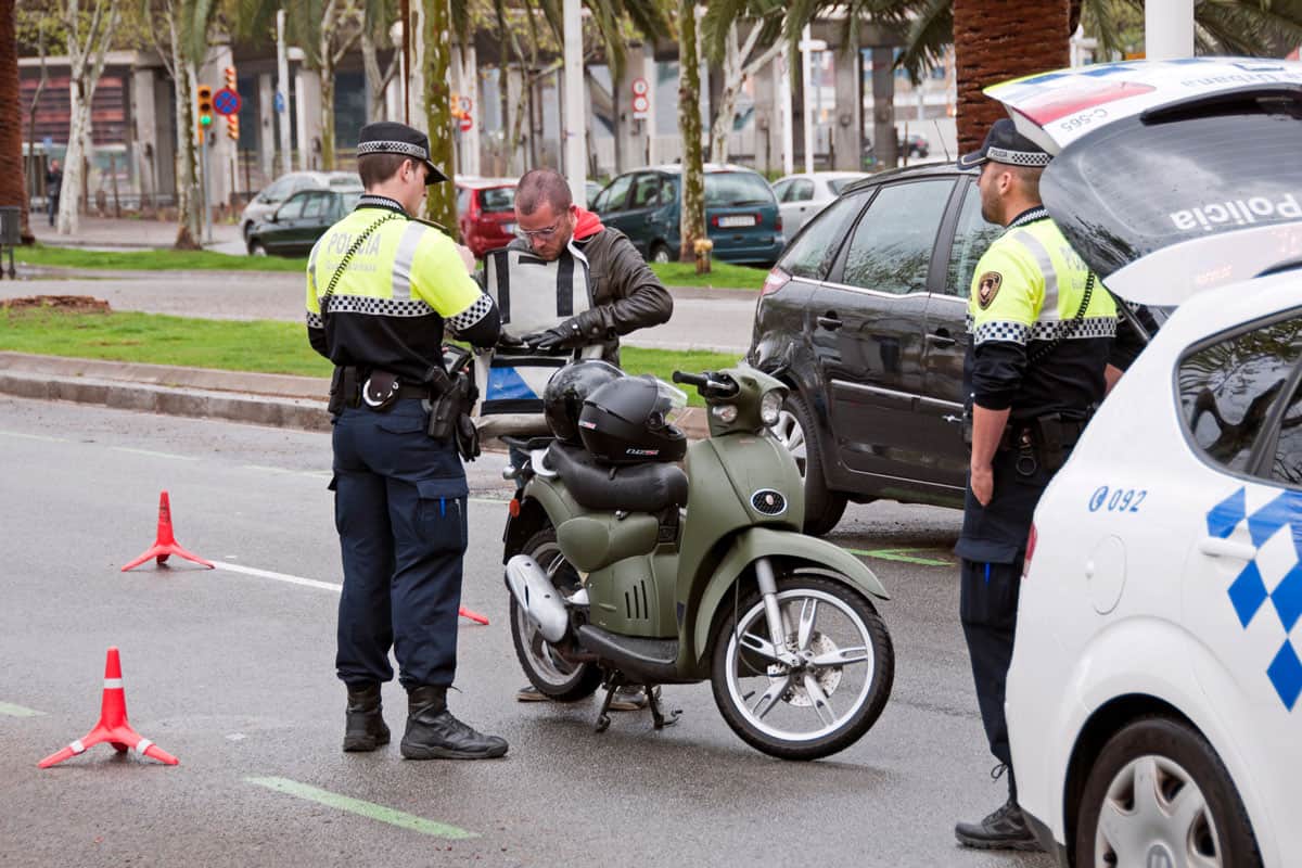 A man riding a motor scooter is detained by police at a random checkpoint for drug and alcohol abuse and license