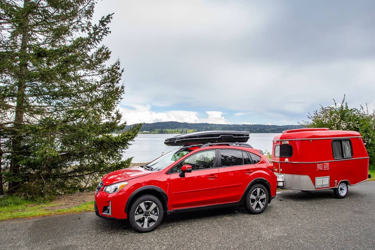 A red car carrying a kayak and towing a teardrop camper