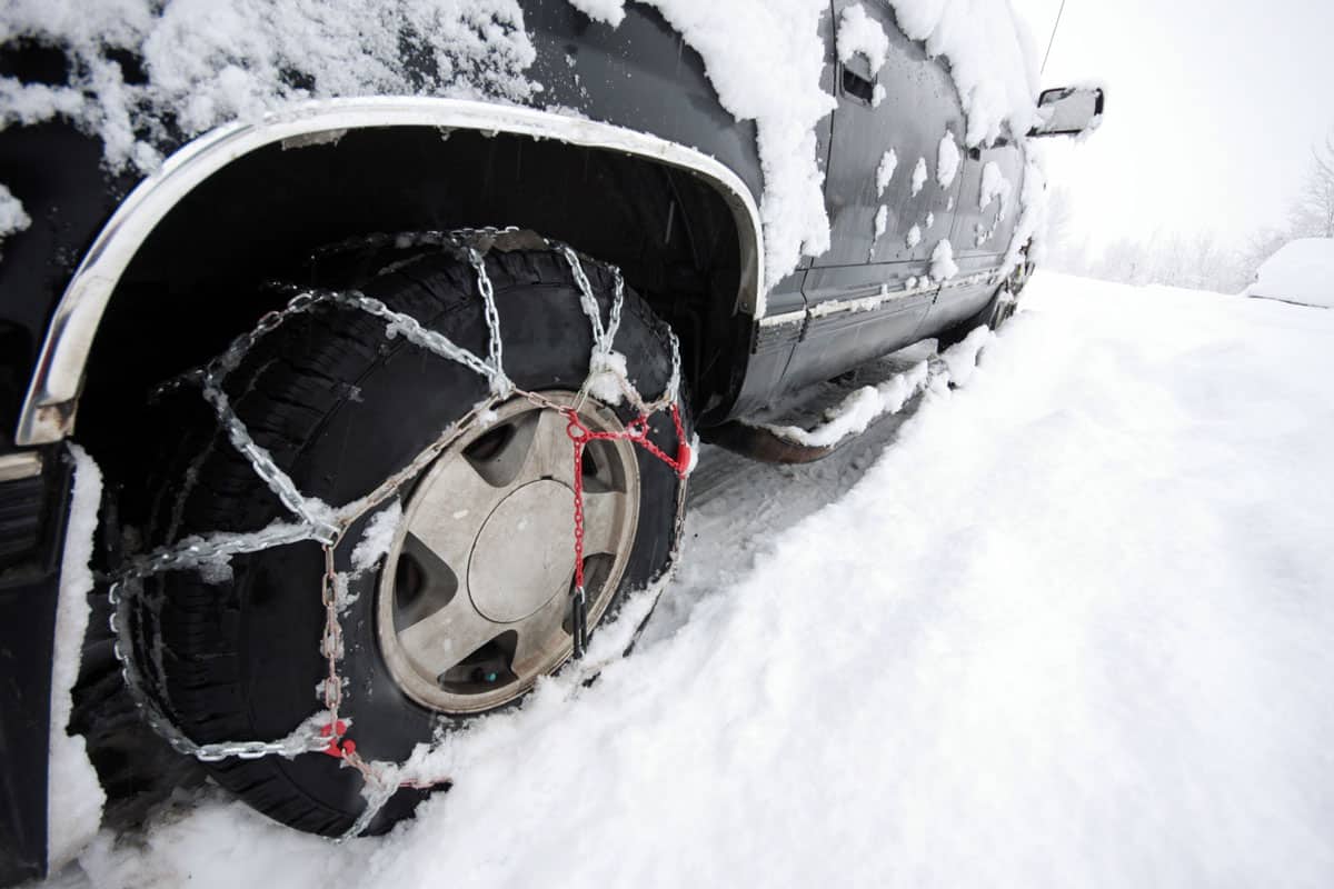 An SUV in the snow with chains on both front and rear tires