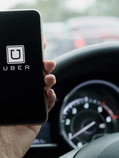 An Uber driver holding Uber app showing on iPhone while driving, Can I Drive For Uber In Another State? [And How To Transfer]