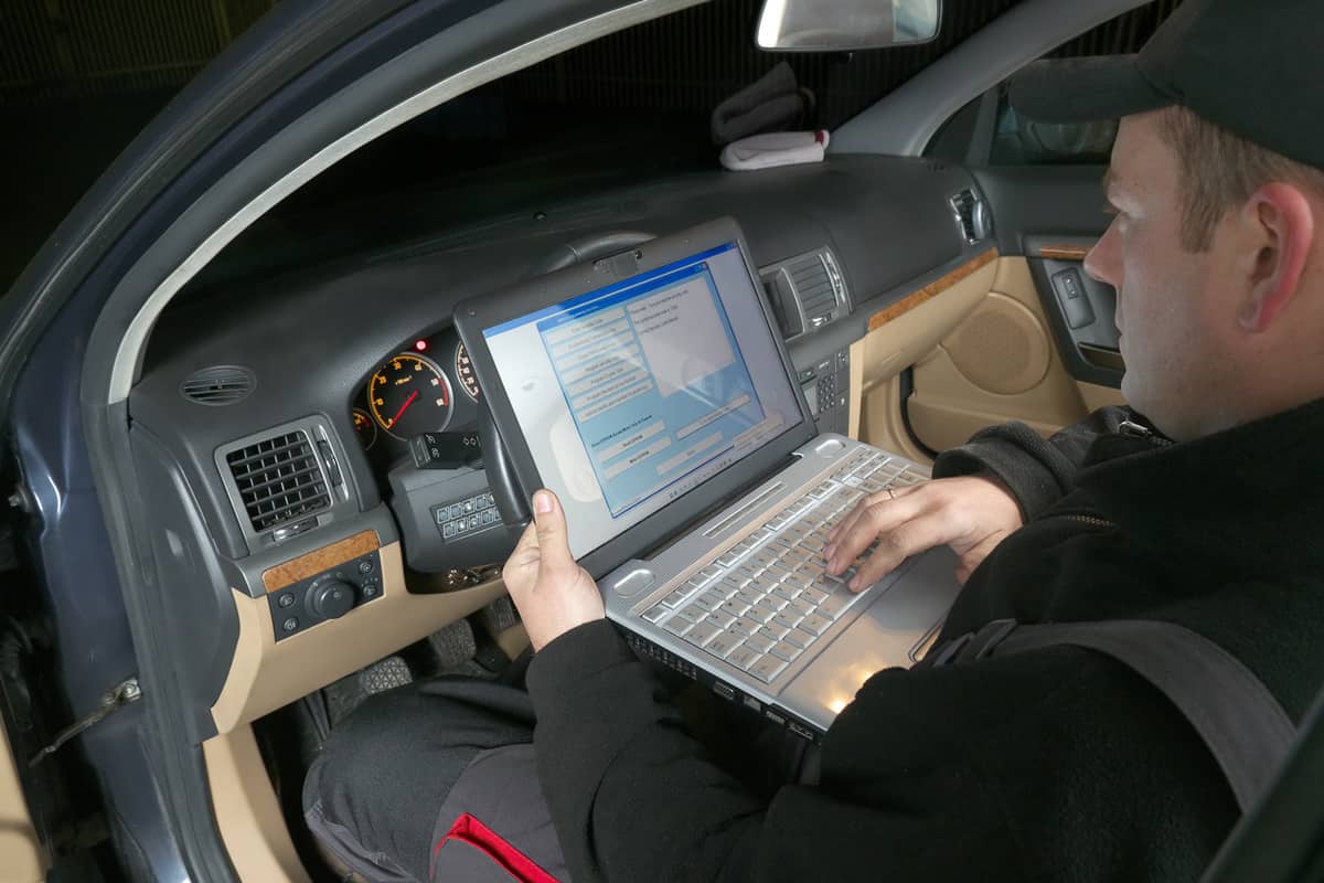 Auto mechanic checking vehicle identification number of the car using laptop hooked up to the car onboard computer